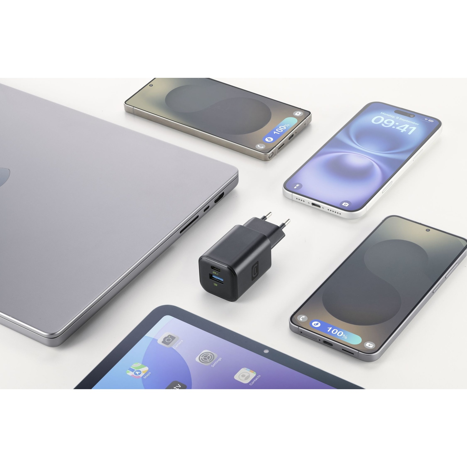 Un laptop, tre smartphone, un caricabatterie e un tablet su una superficie bianca.