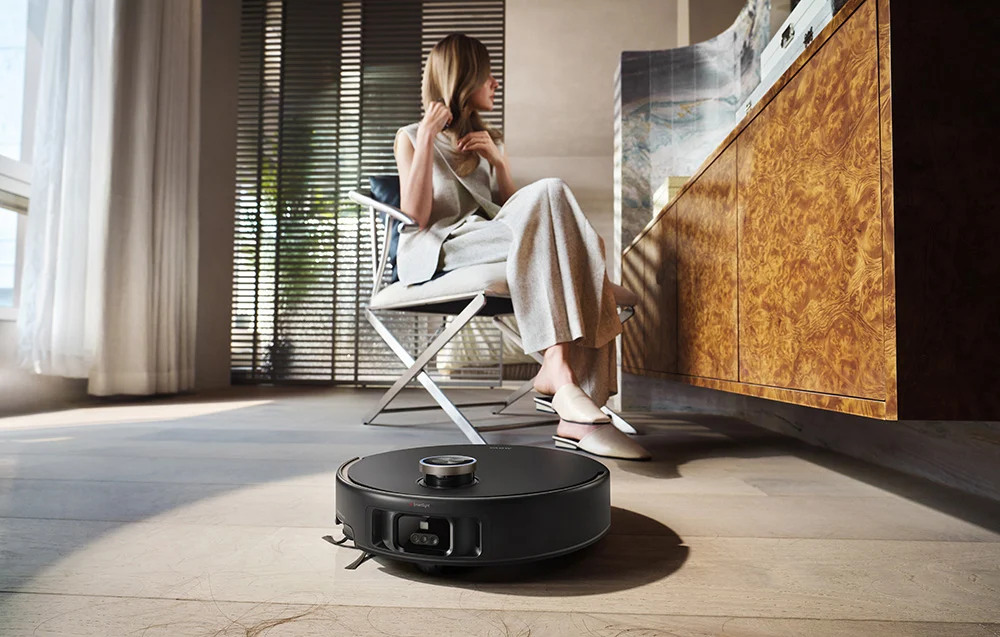 Robotporszívó a fapadlón ülő nő előtt.
