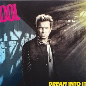 Billy Idol tüskés hajjal komolyan néz a kamerába, dzsekit visel.