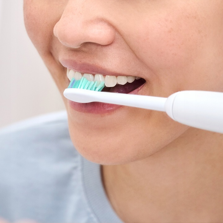 Osoba myje zęby szczoteczką elektryczną.