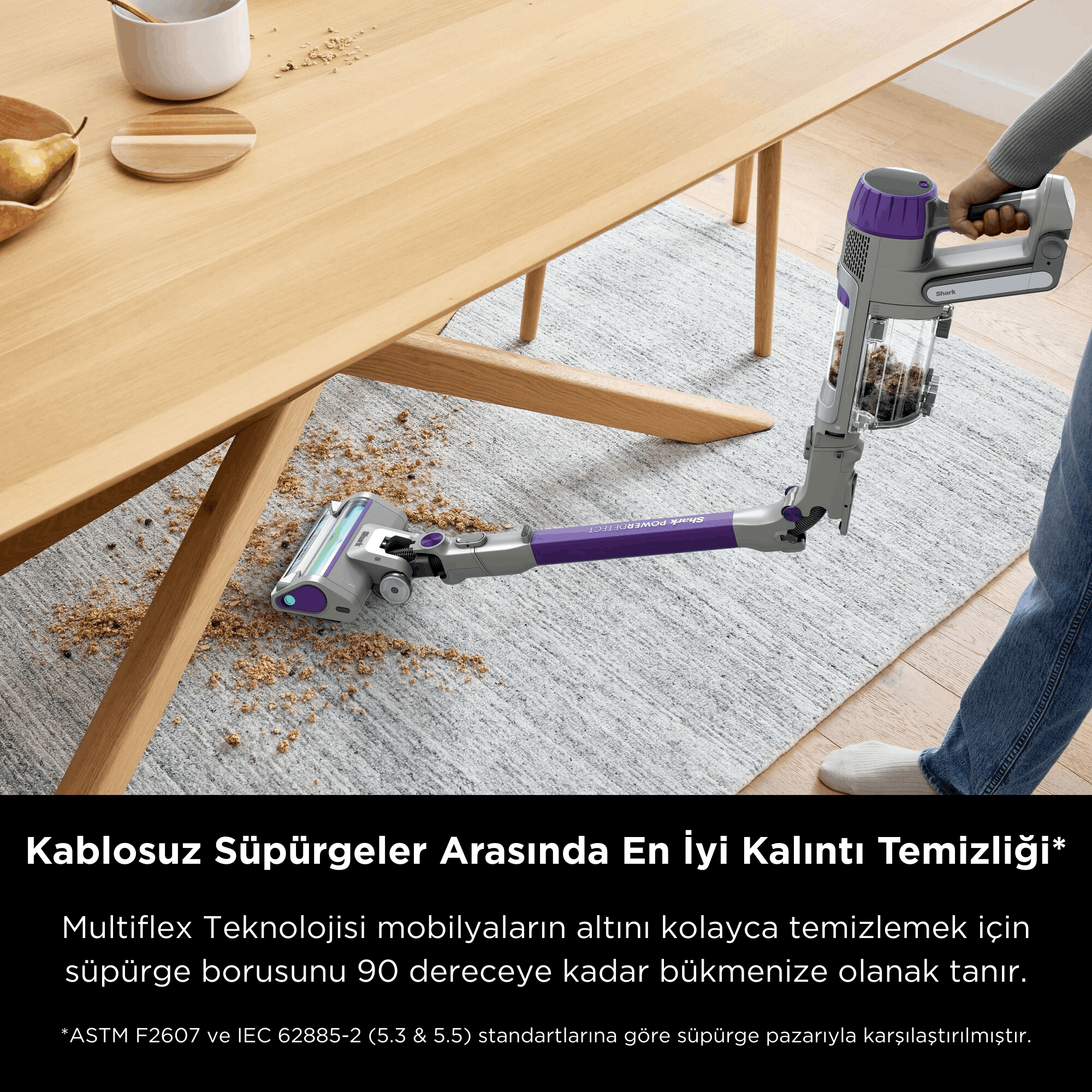Mor renkli süpürge, ahşap masa altındaki halıyı temizliyor.