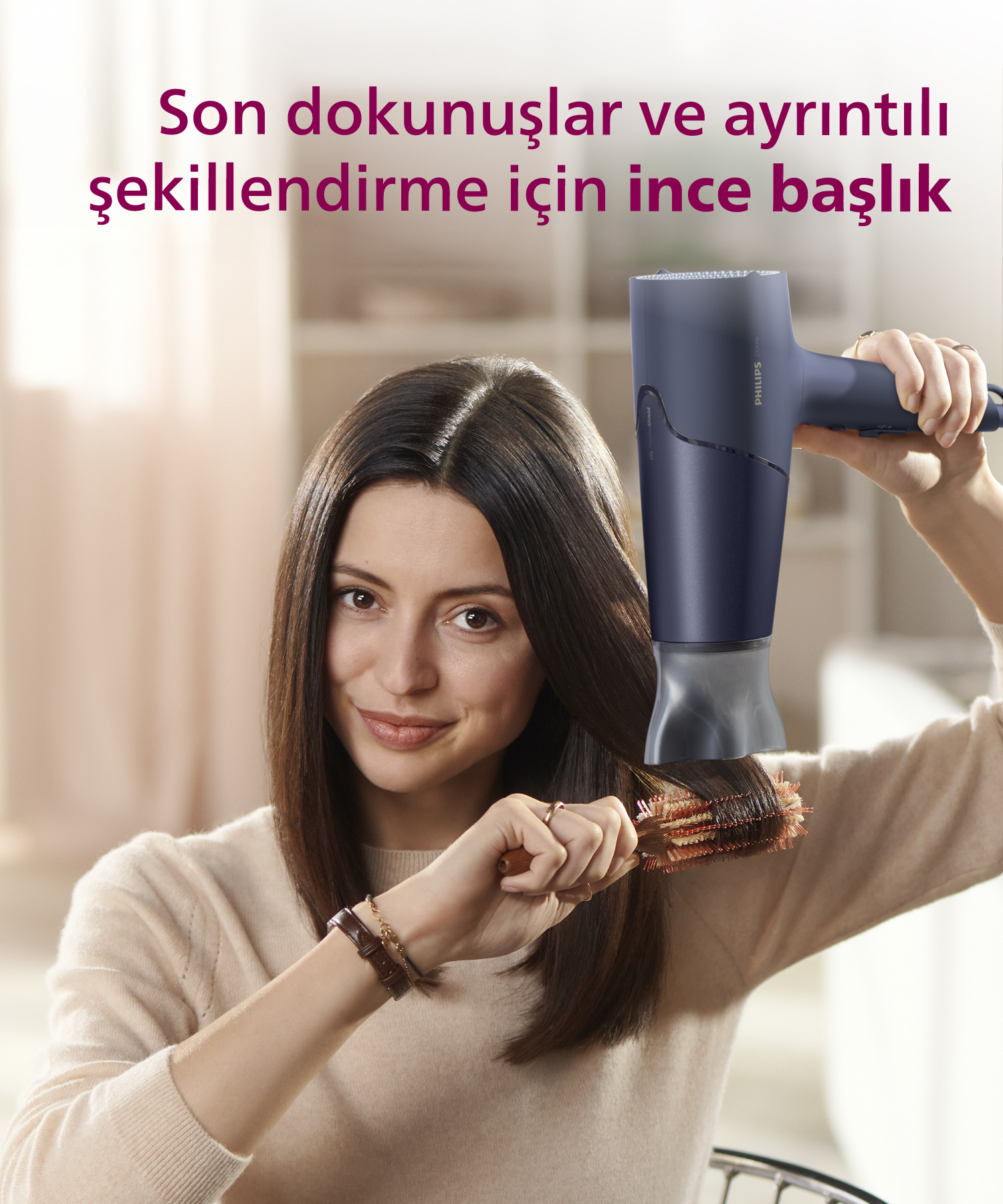 Kadın, mavi saç kurutma makinesi ve yuvarlak fırça ile koyu renk saçlarını şekillendiriyor.