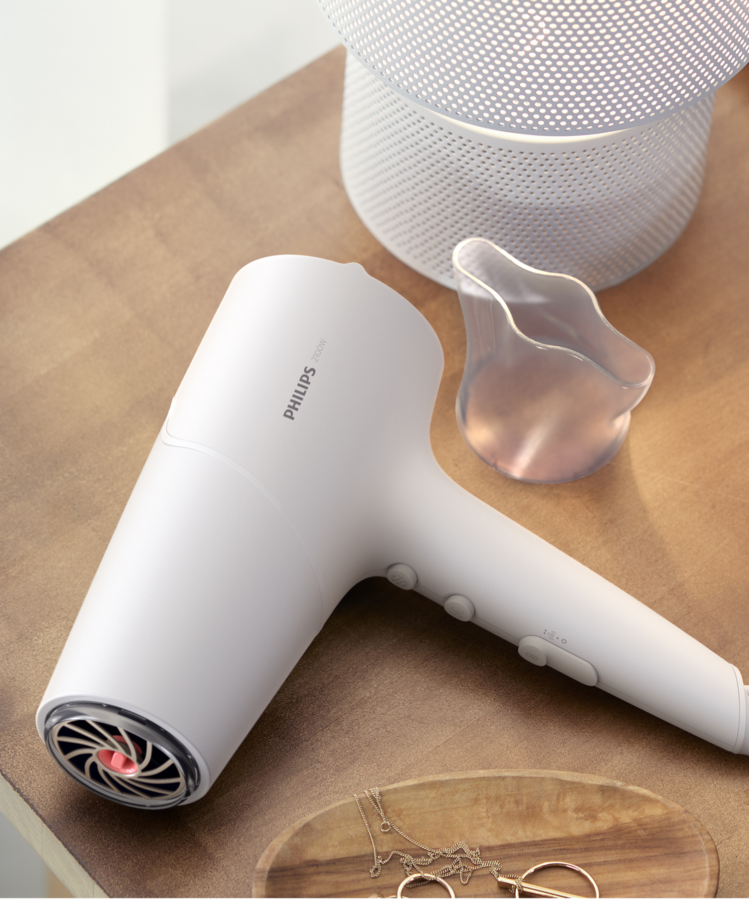 Beyaz bir Philips saç kurutma makinesi, mücevher ve lamba yanında ahşap bir masada duruyor.