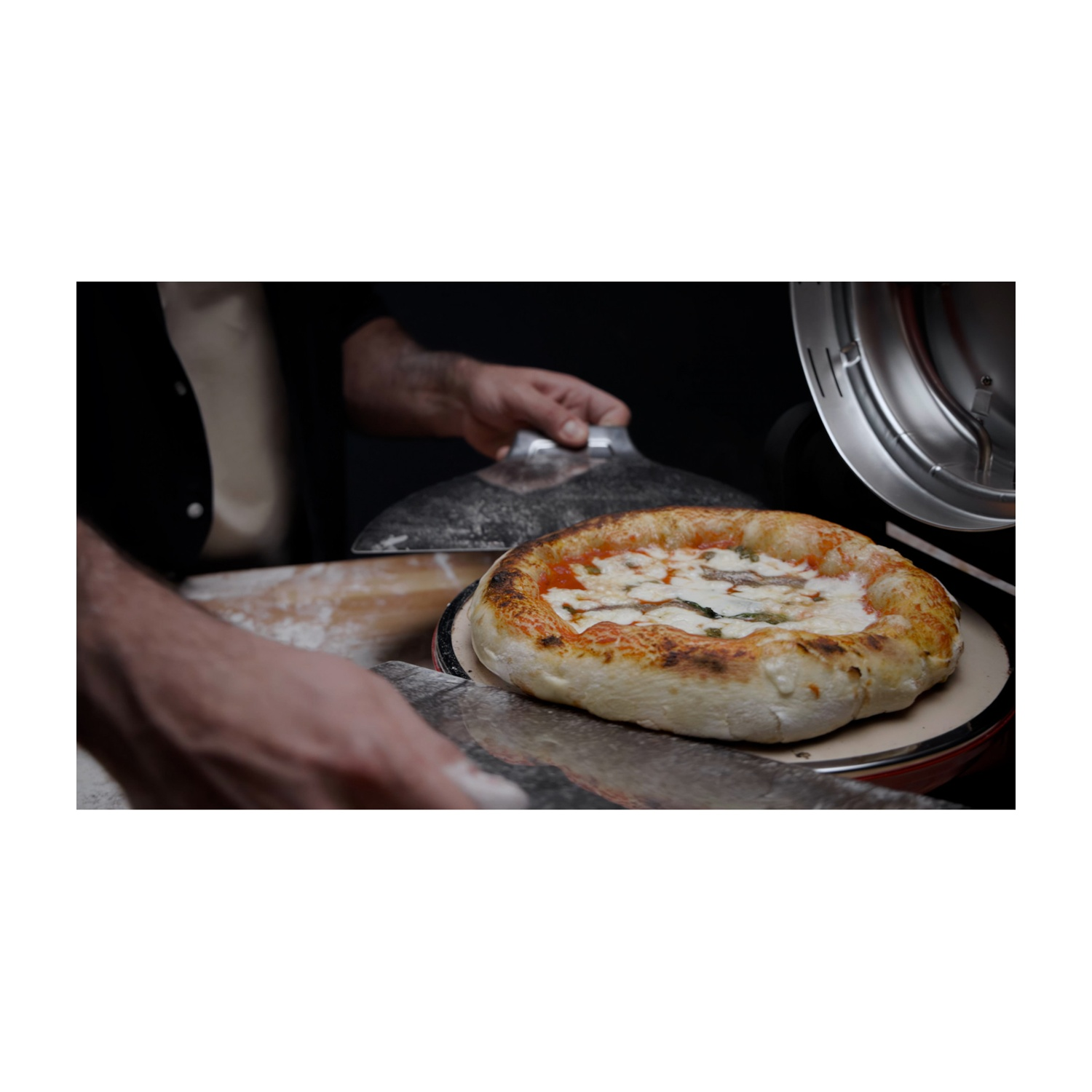 Un pizzaiolo fa scivolare una pizza con mozzarella e acciughe in un forno.