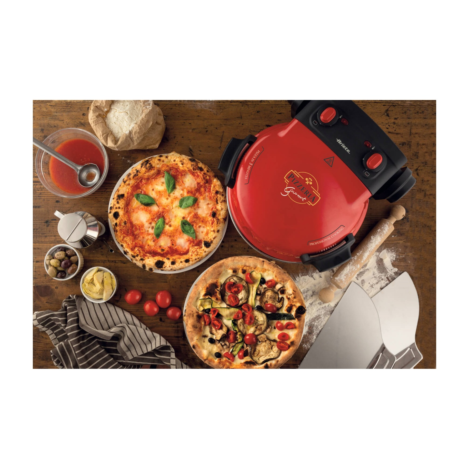 Forno per pizza rosso con due pizze, pomodori, olive, salsa e attrezzi su tavolo di legno.