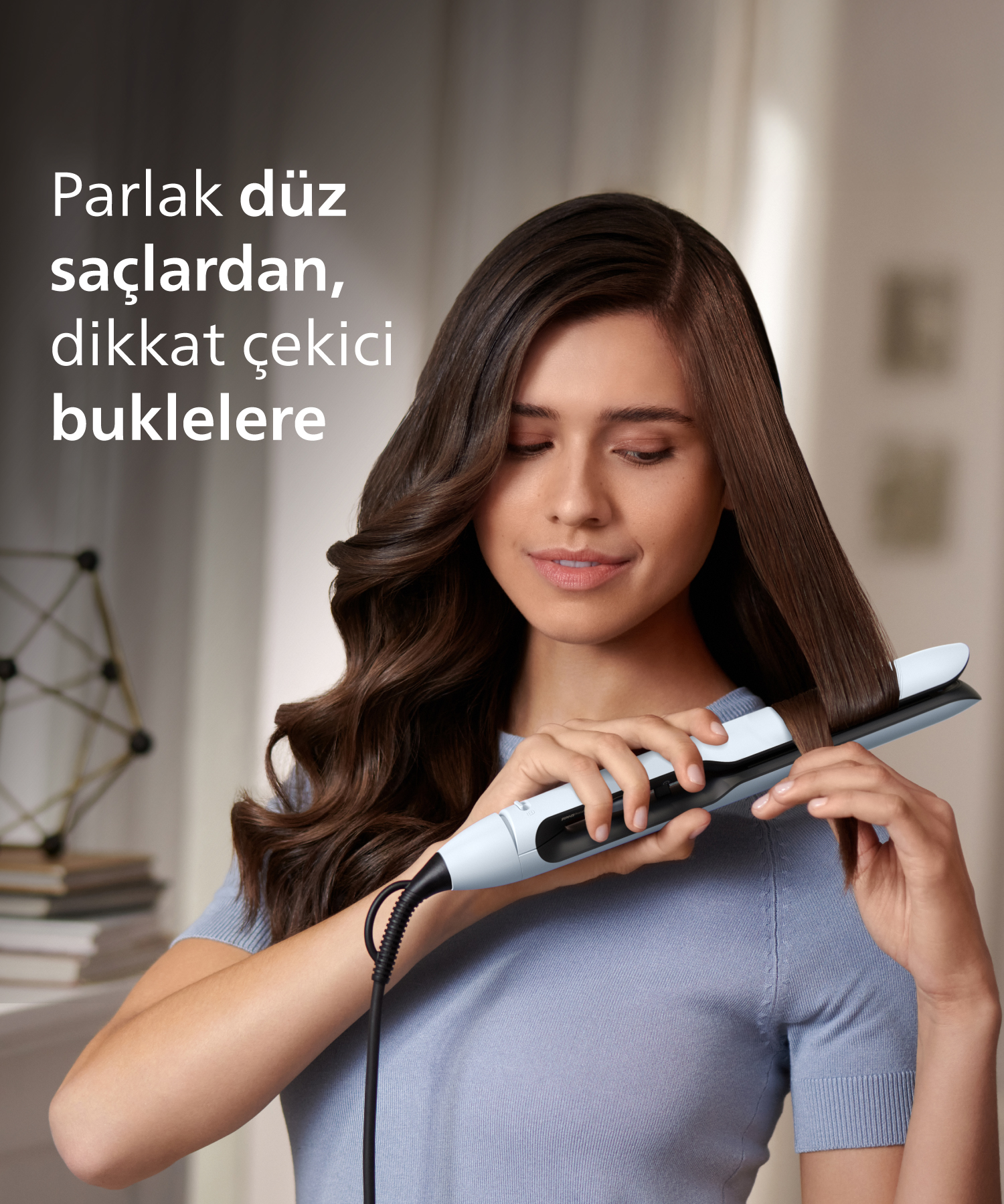 Bir kadın tuttuğu düzleştiriciyle kahverengi saçlarını şekillendiriyor.