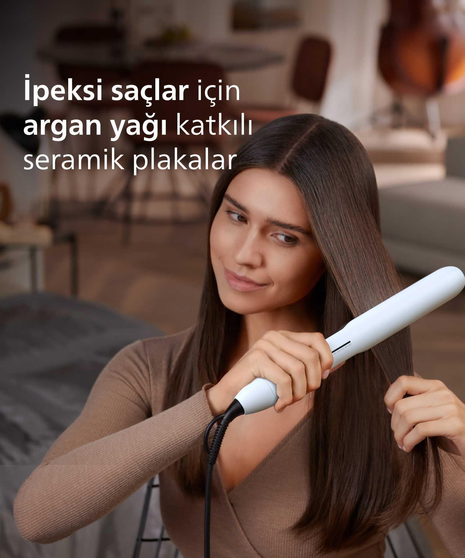 Kadın oturma odasında beyaz düzleştirici ile kahverengi saçlarını düzleştiriyor.