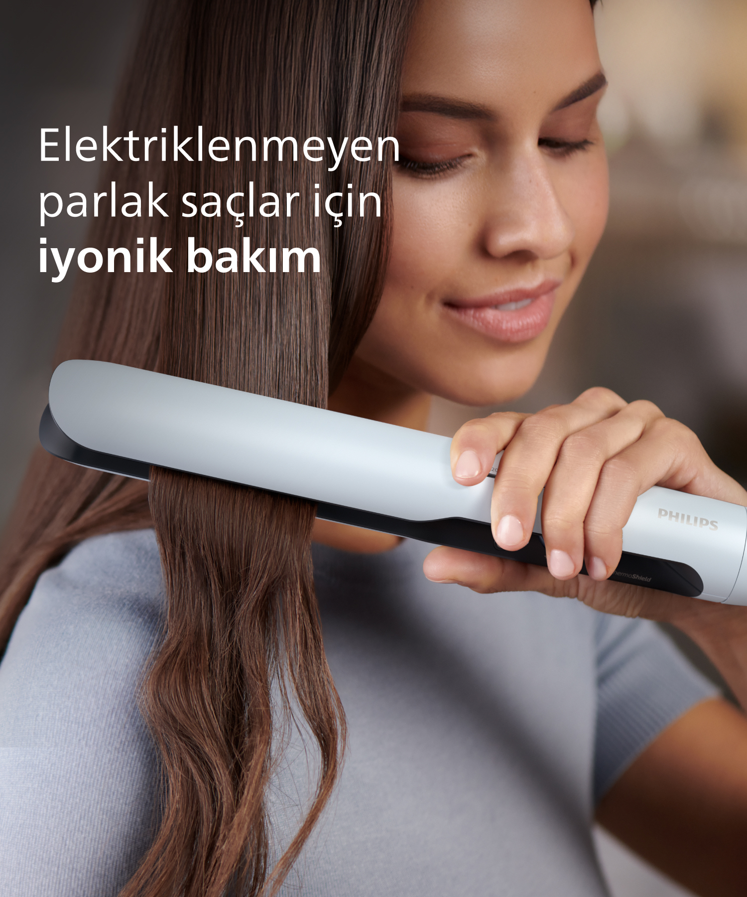 Kadın, kahverengi saçını düzleştirici ile düzleştiriyor.