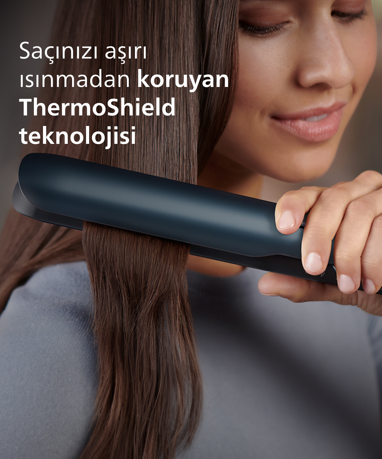 Kadın koyu renk saç düzleştirici ile kahverengi saçını düzleştiriyor. Türkçe metin.