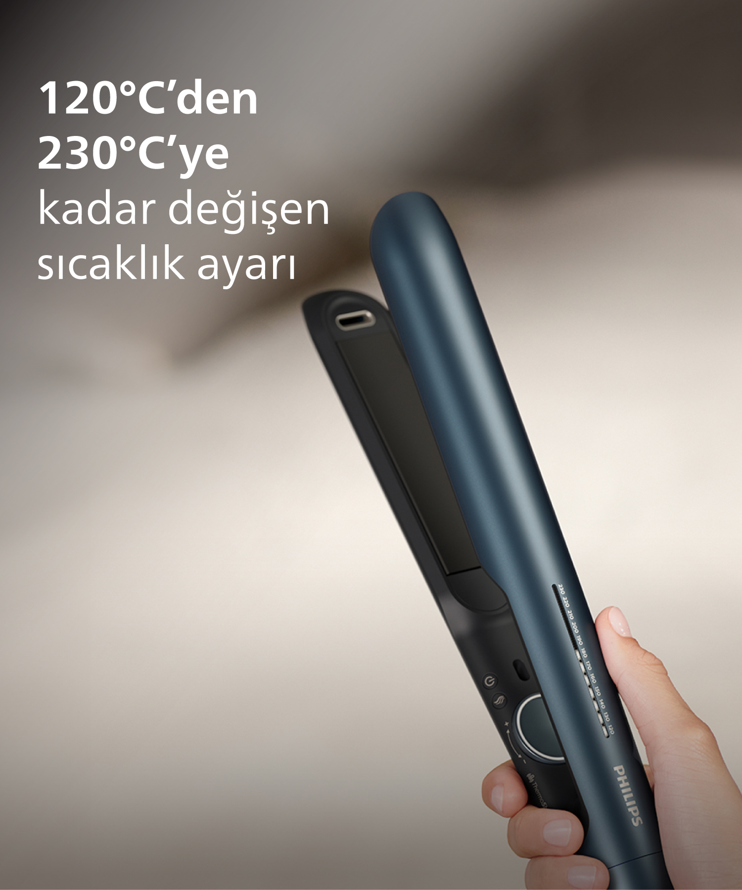 Bir el, 120-230°C ayarlanabilir sıcaklığa sahip koyu renkli Philips saç düzleştirici tutuyor.