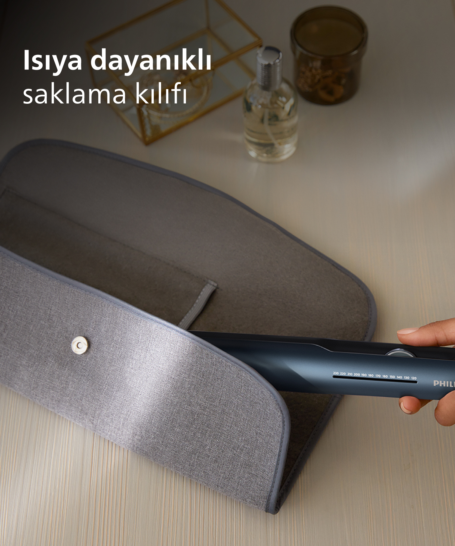 Bir el, gri kumaş kılıfa yerleştirilen koyu renkli saç düzleştirici tutuyor.
