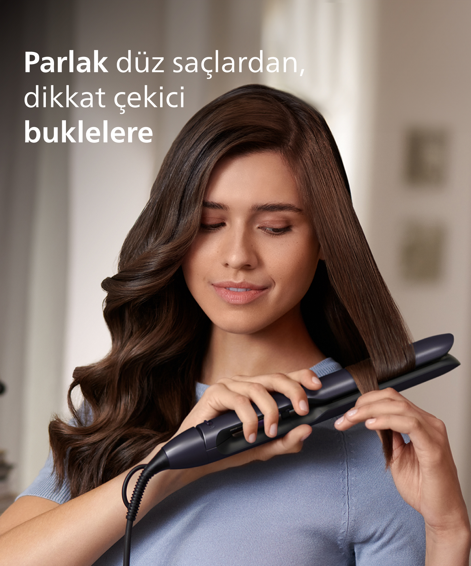 Kahverengi saçlı kadın, kıvırcık saçlar yapmak için saçını düzleştiriciyle şekillendiriyor.