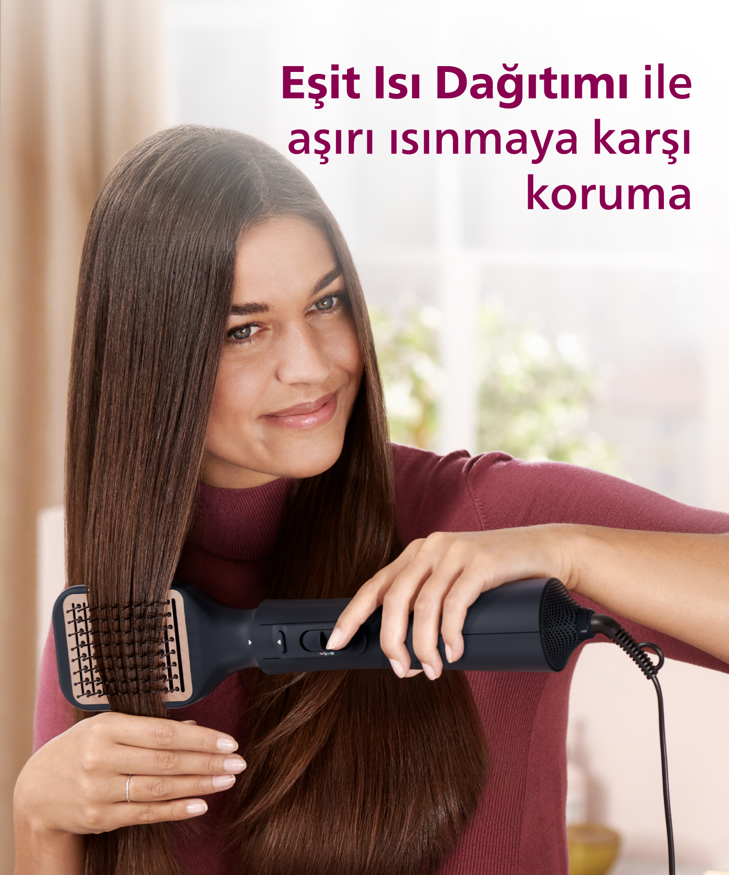 Kadın, uzun kahverengi saçlarını fırça aparatlı siyah saç kurutma makinesiyle şekillendiriyor.