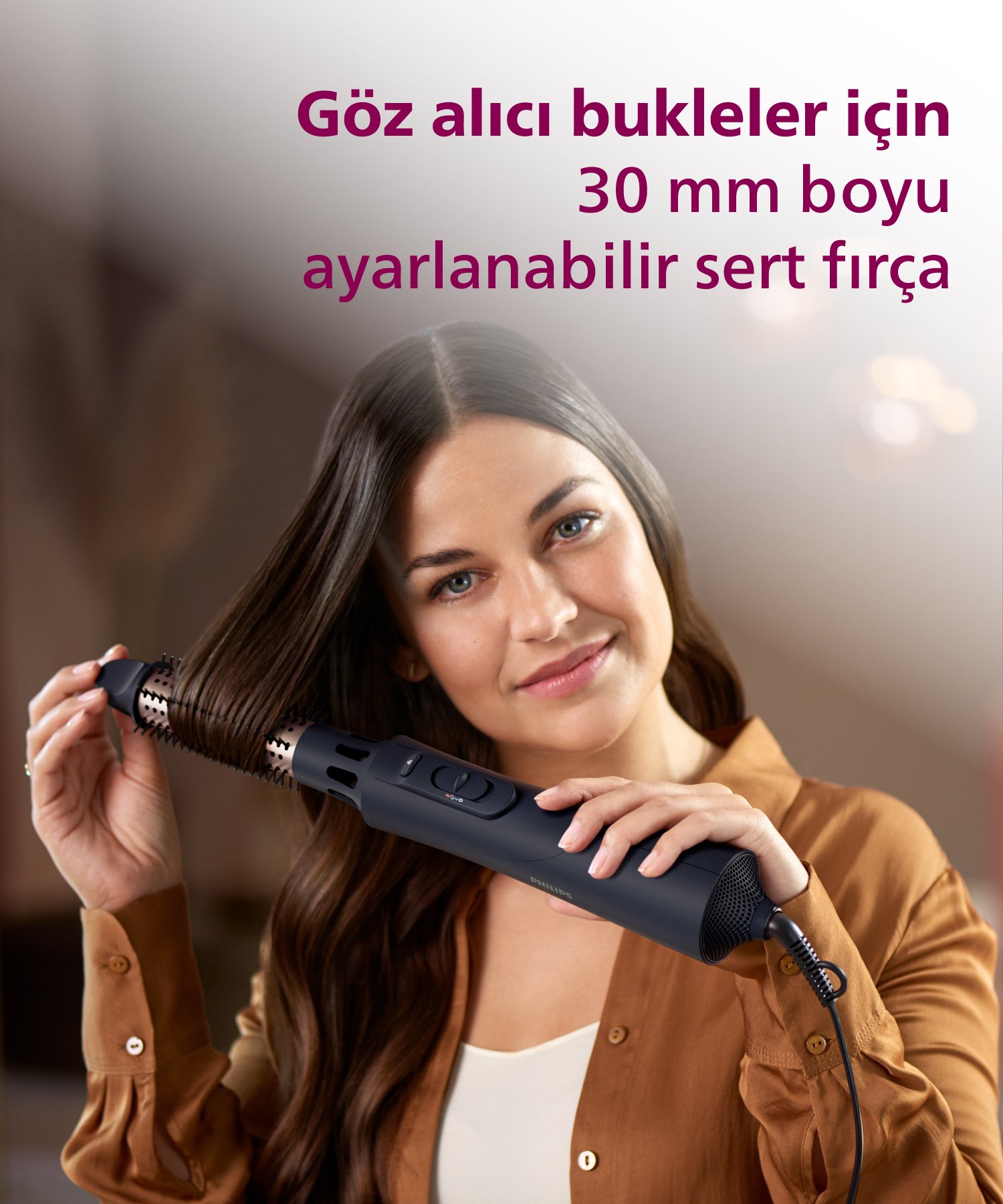 Uzun saçlı bir kadın, saçını şekillendirmek için Philips döner fırça kullanıyor.