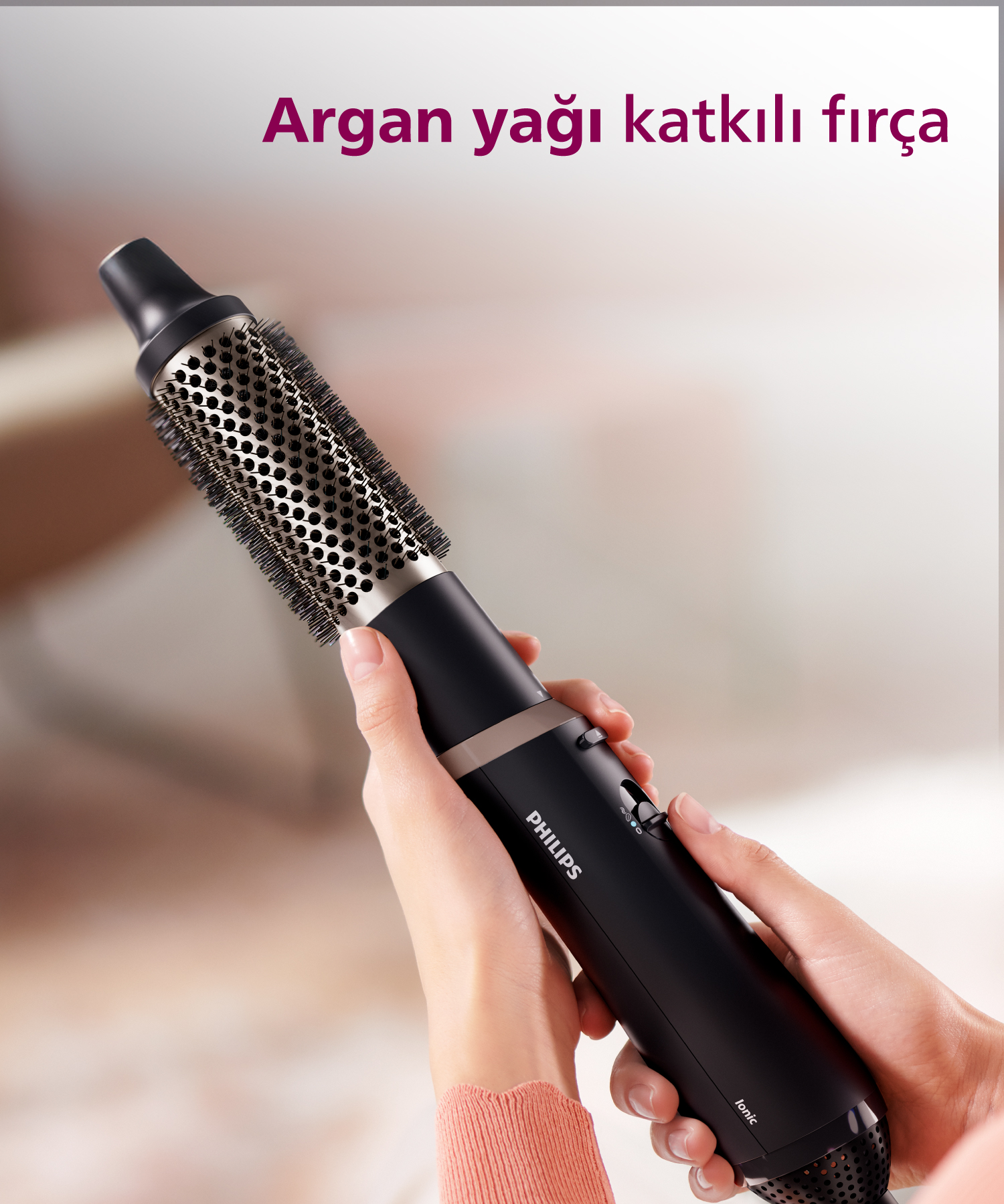 İki el tarafından tutulan, fırça aparatlı siyah Philips saç kurutma makinesi.