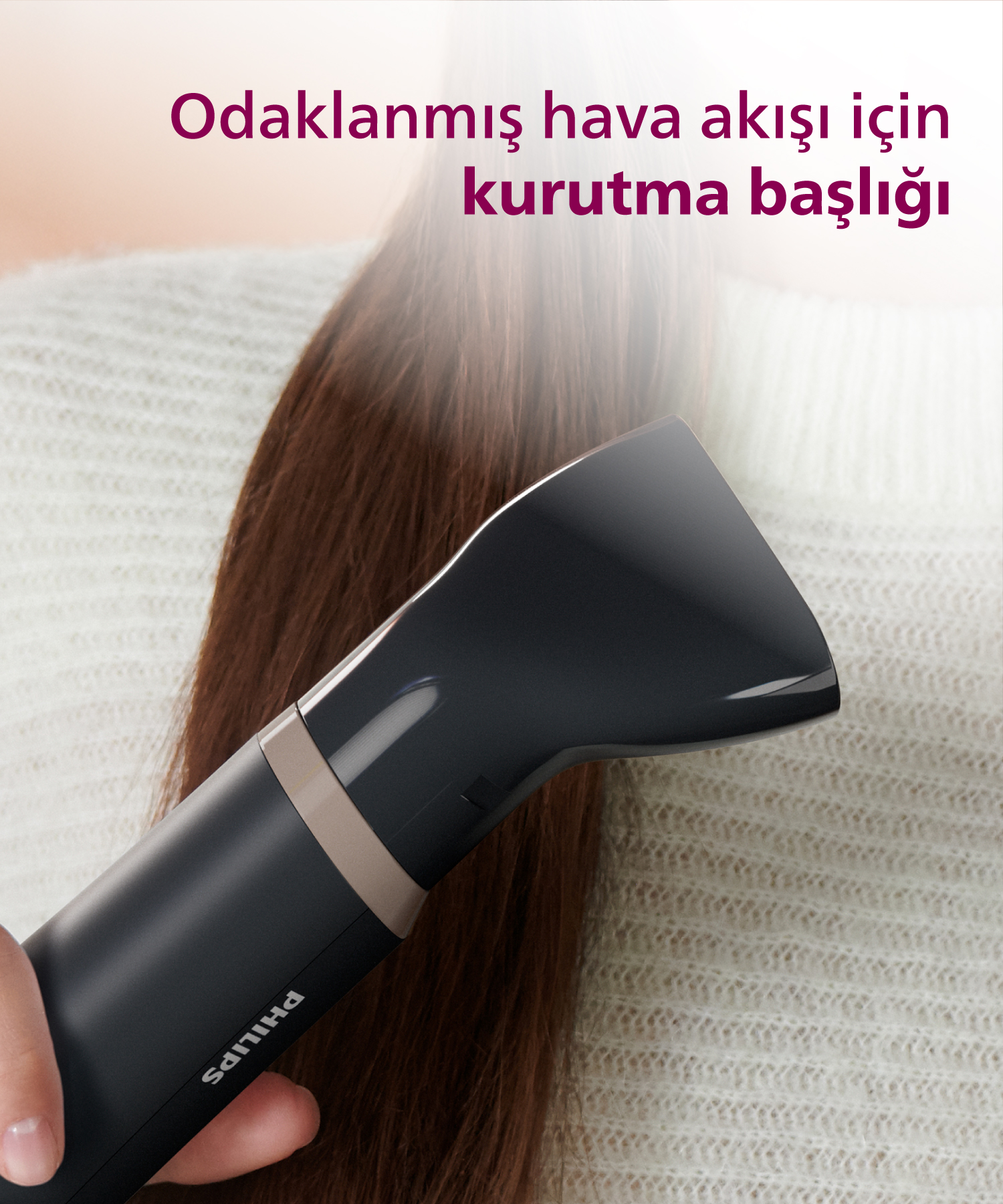 Siyah Philips saç kurutma başlığı kahverengi saç kurutuyor. Arkada beyaz örgü kazak.