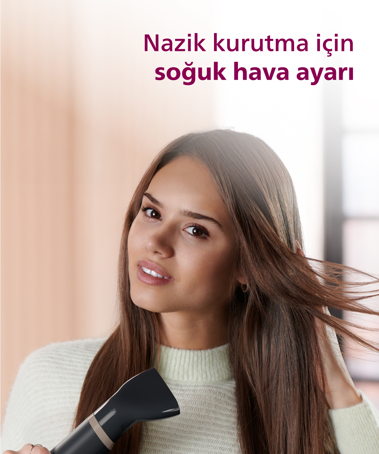Kahverengi saçlı genç bir kadın, siyah saç kurutma makinesiyle saçını kurutuyor.