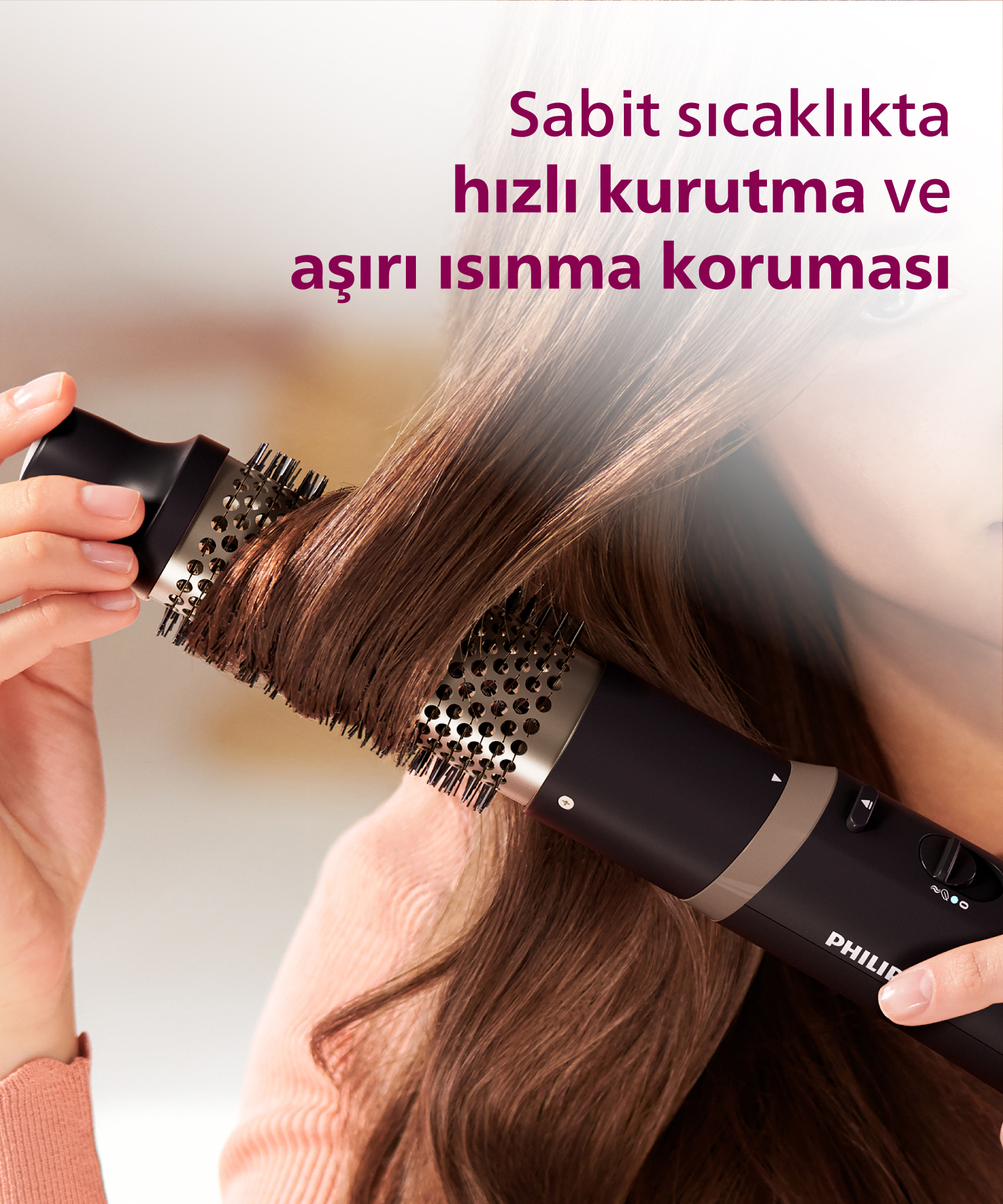 Bir el, kahverengi saçı şekillendirmek için yuvarlak fırçalı siyah saç kurutma makinesi kullanıyor.