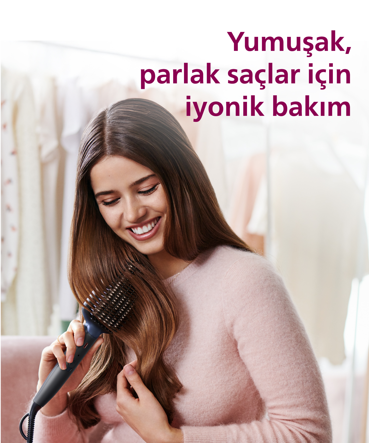 Kadın, elektrikli fırçayla saçını tararken gülümsüyor, memnun görünüyor.