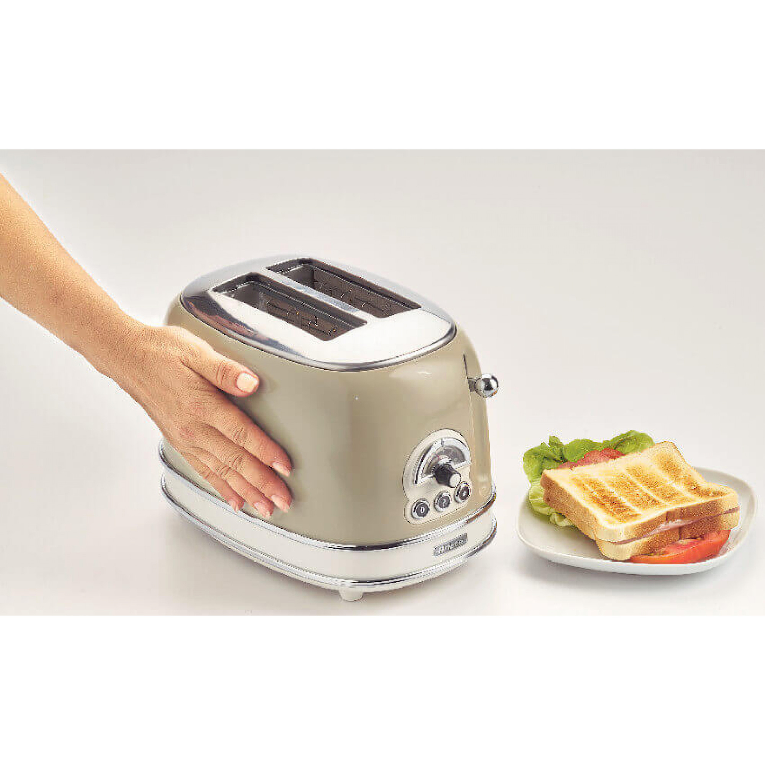 Un tostapane beige con una mano sopra, e un piatto con un sandwich accanto.