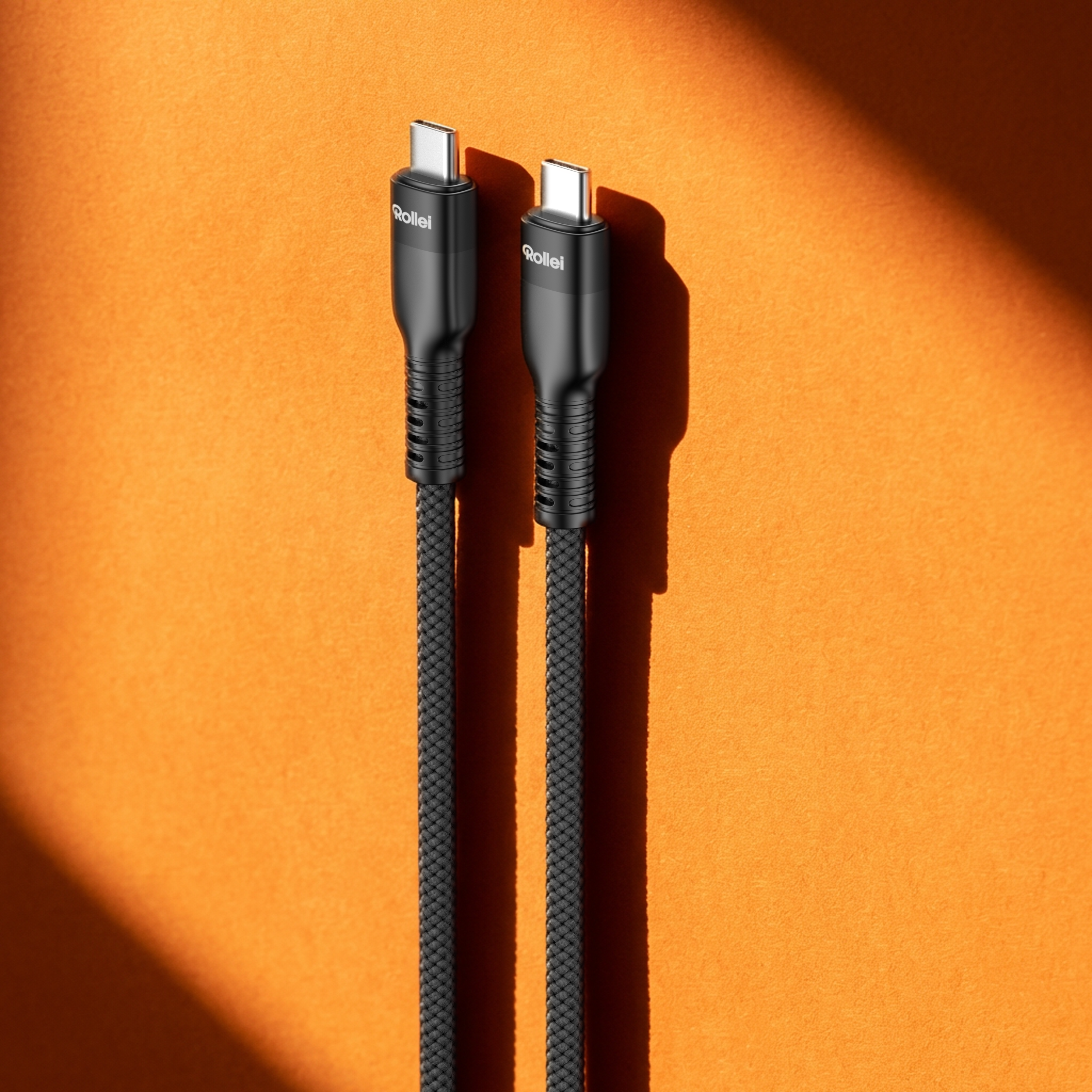 Zwei schwarze Rollei USB-C-Kabel auf orangefarbenem Hintergrund mit Schatten.