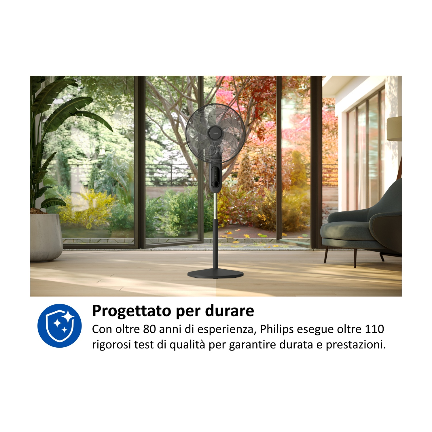 Un ventilatore nero da terra in una stanza luminosa con grandi finestre e piante.