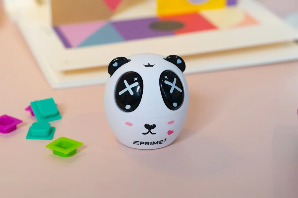 Ostrzałka do ołówków w kształcie pandy z oczami w krzyżyki na różowym biurku.