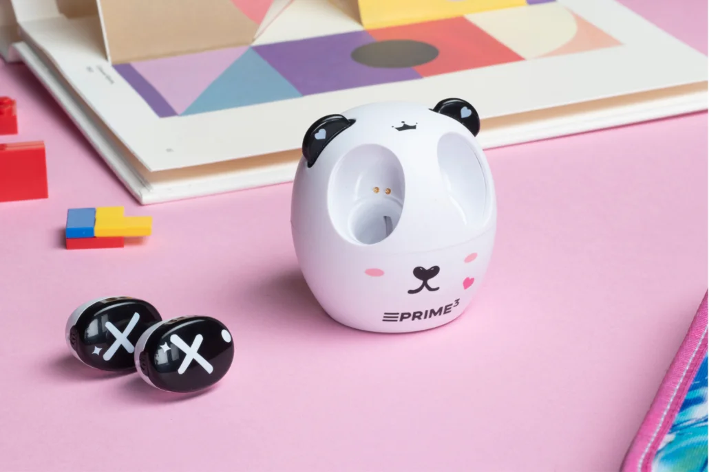 Białe urządzenie w kształcie pandy na różowym tle z dwoma czarnymi słuchawkami i klockami.