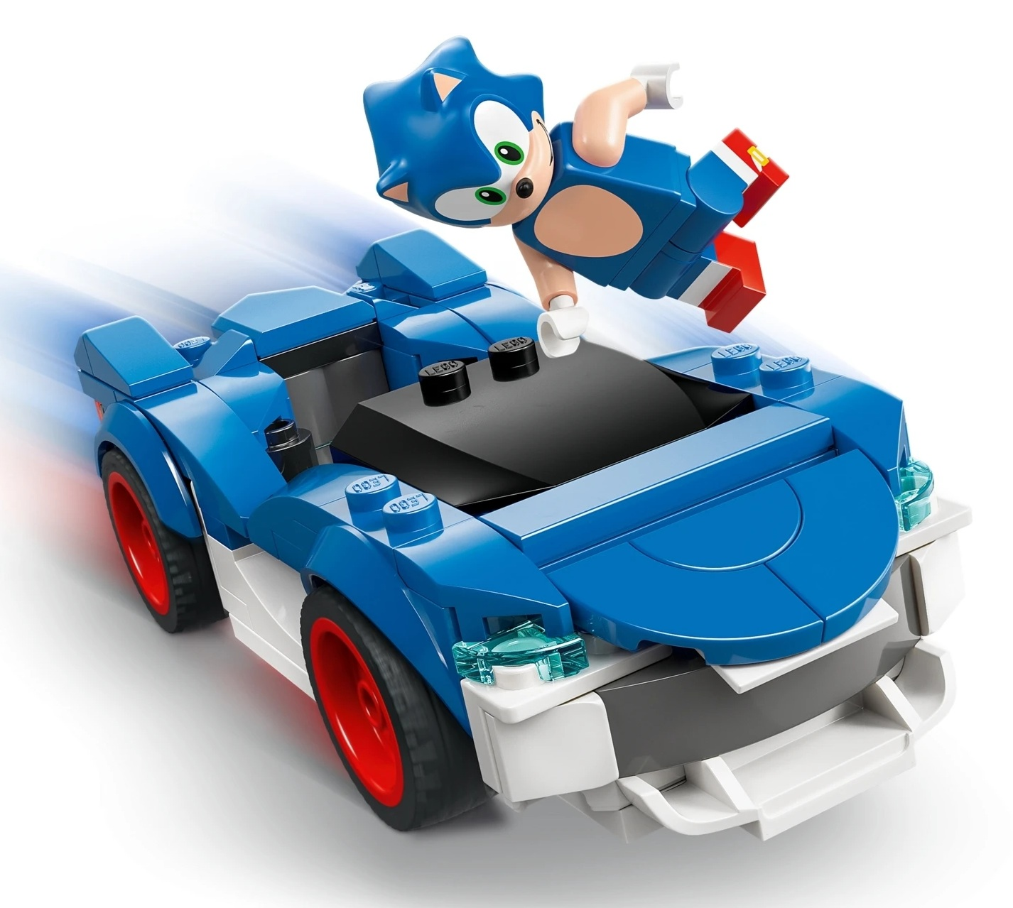 Figurka Sonic the Hedgehog skacze nad niebieskim samochodem Lego z czerwonymi kołami. Rozmycie ruchu wskazuje prędkość.