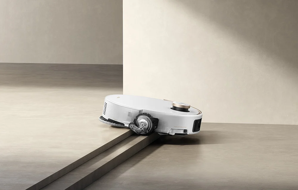 Egy fehér robotporszívó rámpán navigál, minimalista háttérrel.