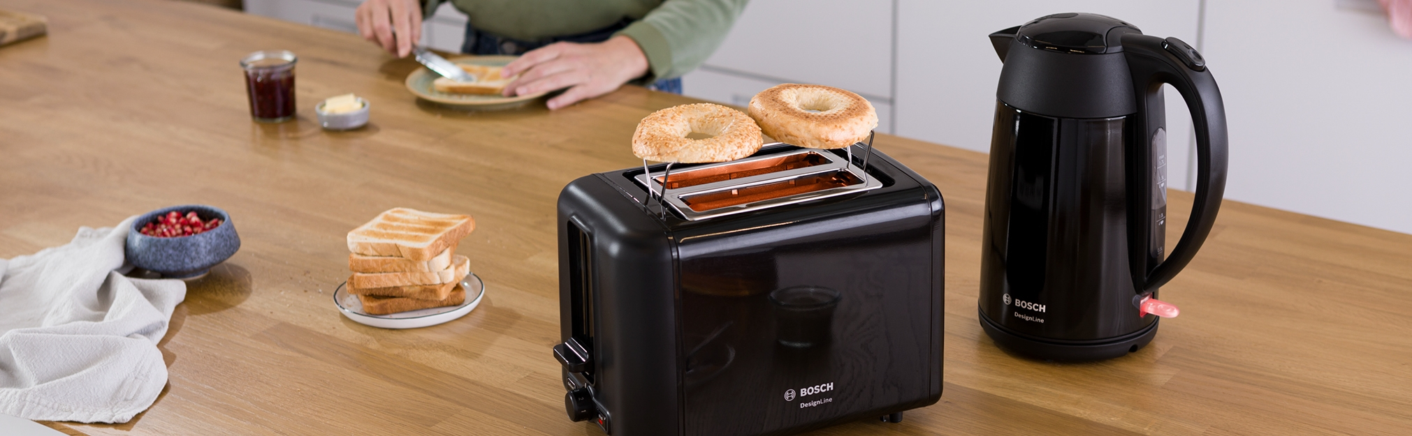 Czarny toster z bajglami, tostami, pestkami granatu i czajnikiem na blacie.