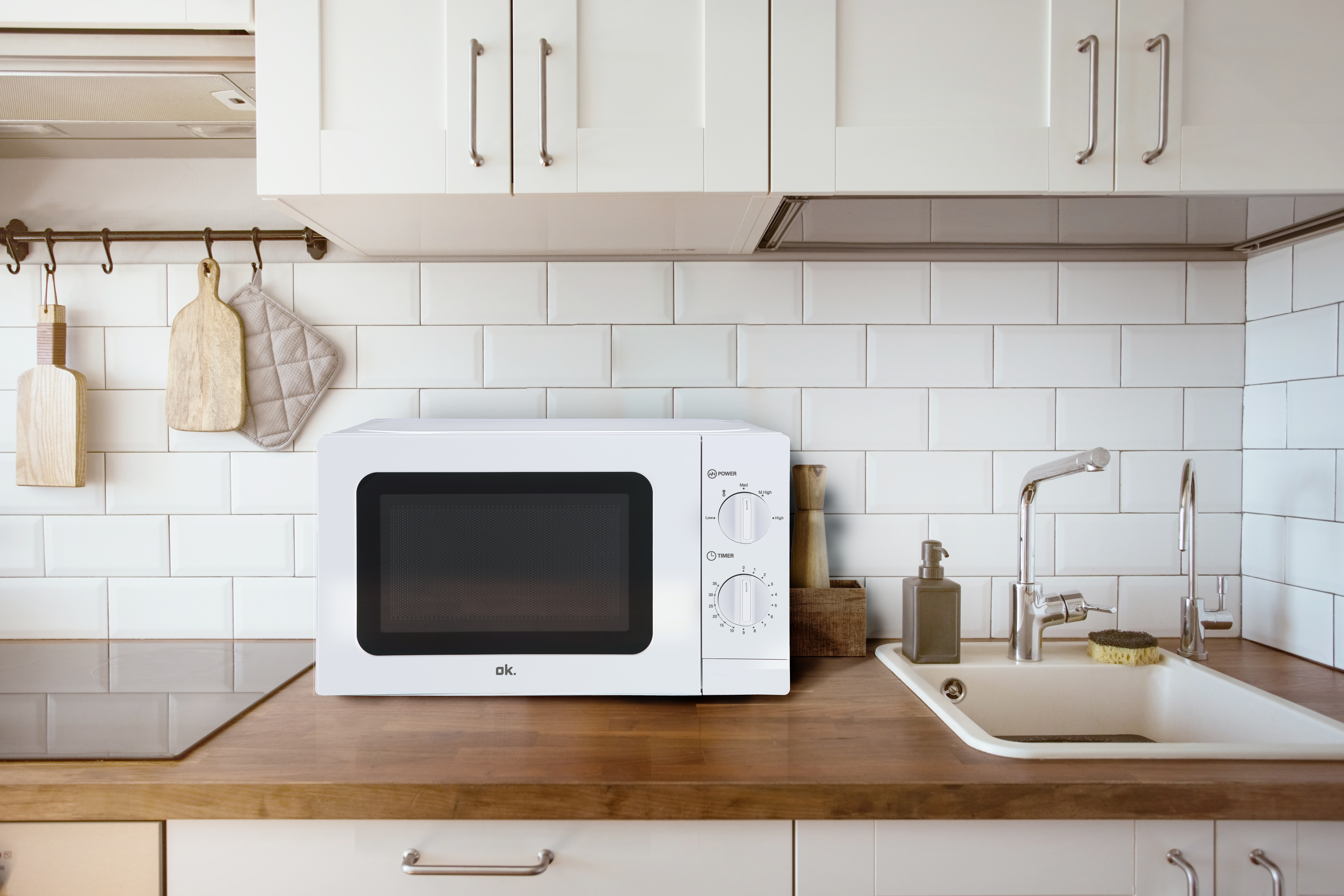 Biała kuchenka mikrofalowa na drewnianym blacie obok zlewu i kranów.