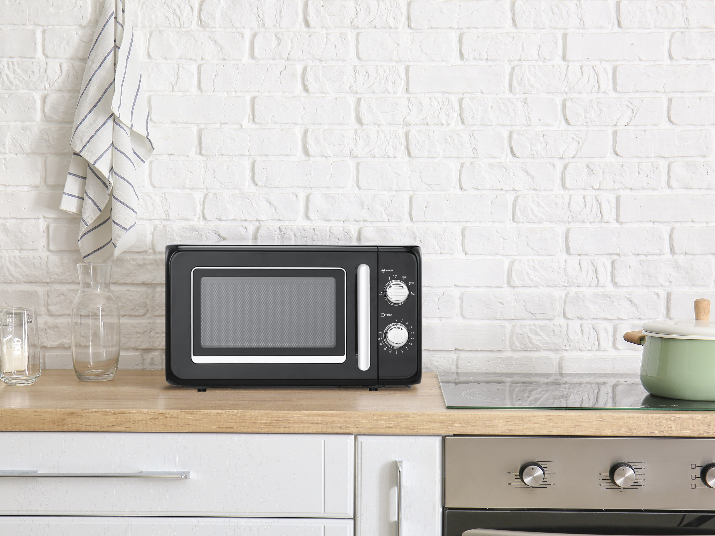 Czarna kuchenka mikrofalowa stoi na blacie obok zielonego garnka.