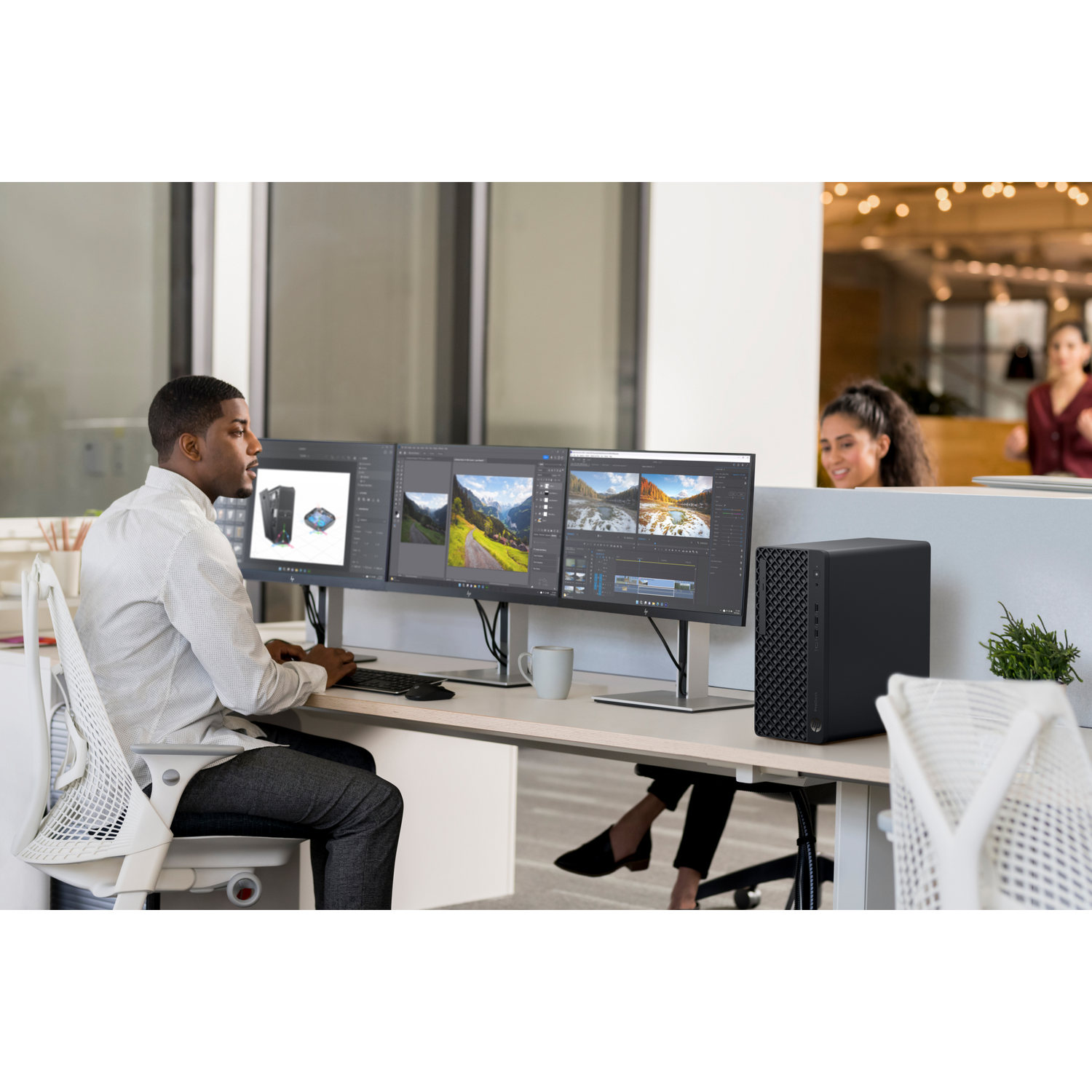 Man works at a desk with three monitors and a black computer.