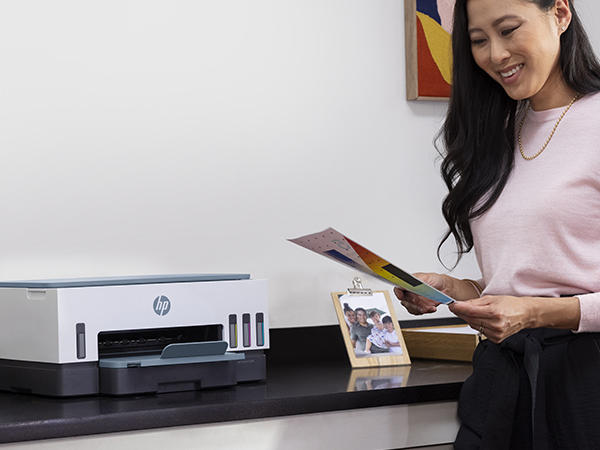 Kobieta ogląda wydrukowane dokumenty obok drukarki HP.