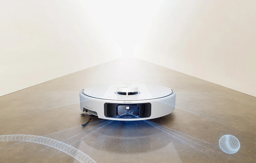Egy fehér robotporszívó betonpadlón kék lézersugarakat bocsát ki.