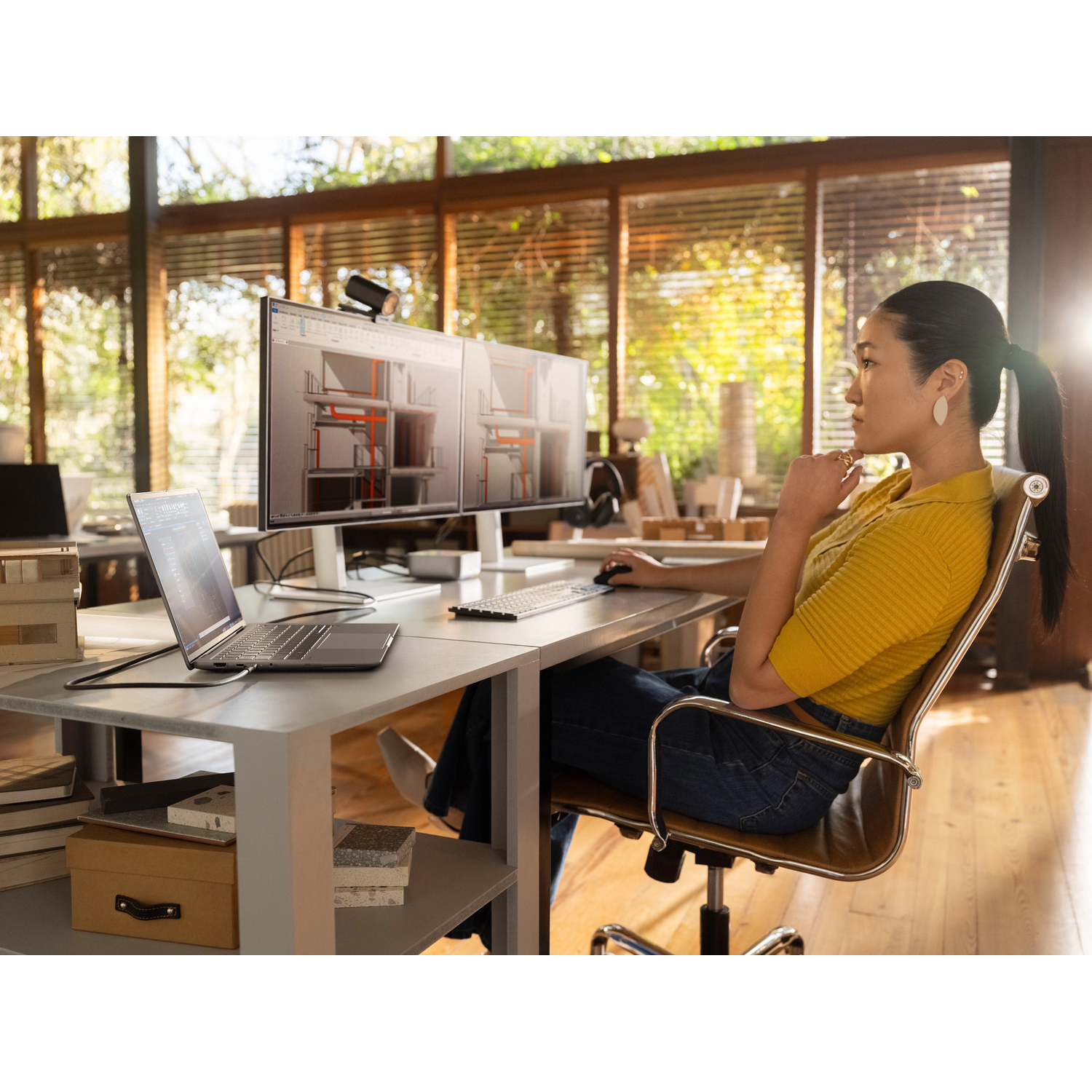 Woman in yellow top at desk with dual monitors, laptop, and mouse.