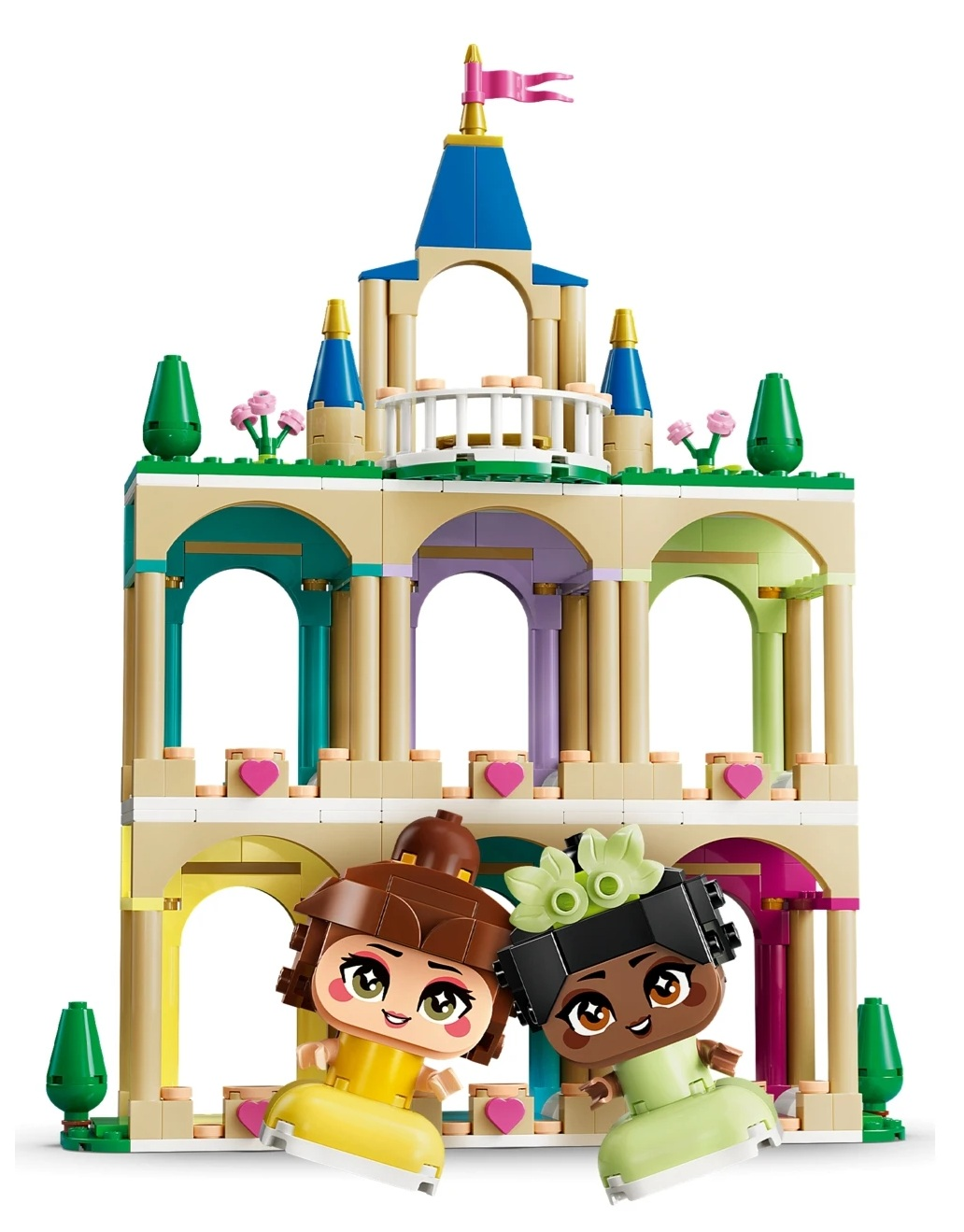 Dwie księżniczki Lego przed kolorowym zamkiem z wieżyczkami i flagą.