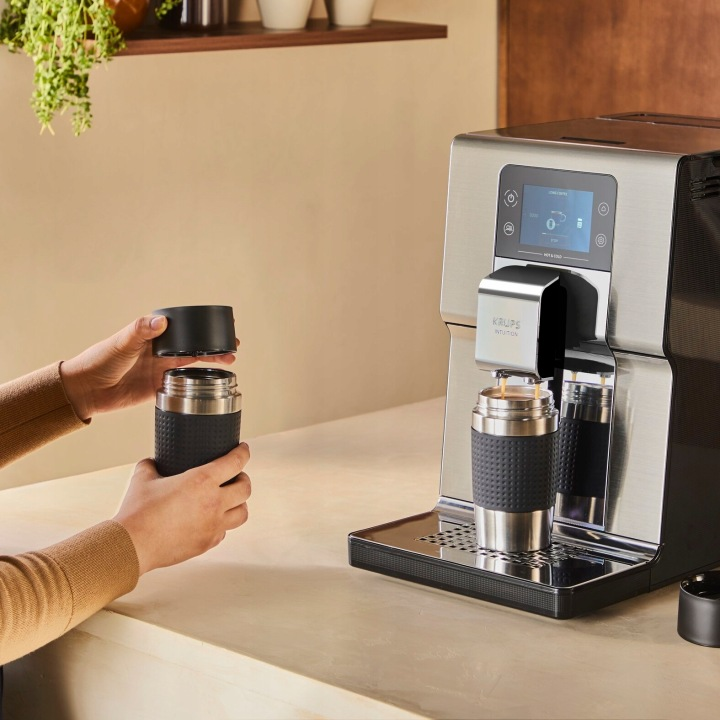 Osoba zakłada pokrywkę na kubek termiczny obok ekspresu do kawy.