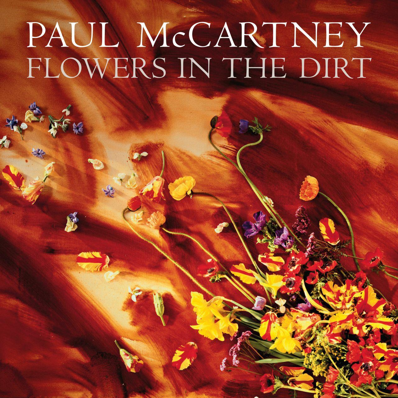 Paul McCartney Flowers in the Dirt albumhoes met verspreide kleurrijke bloemen op een getextureerde oranje achtergrond.