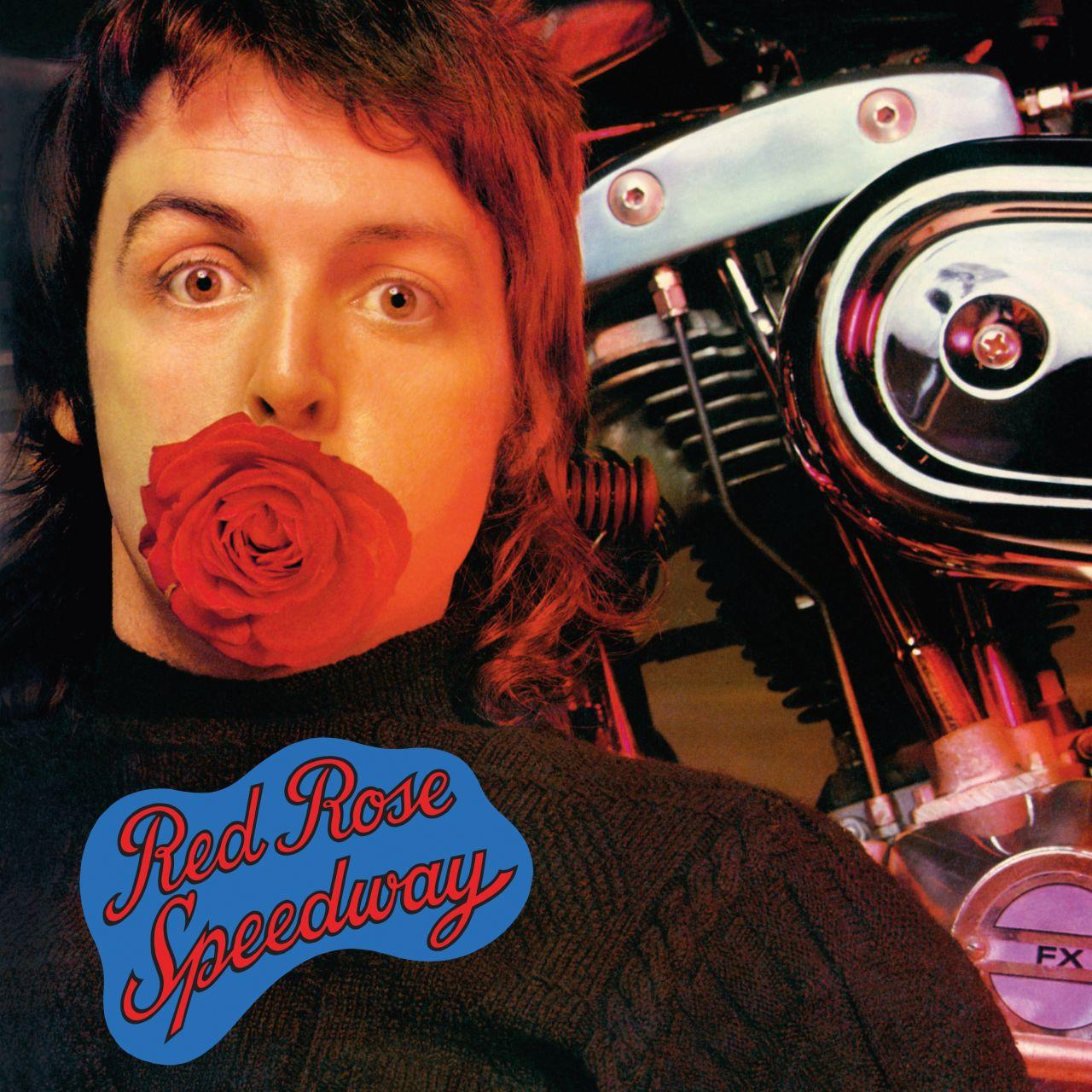 Man met rode roos in mond, naast motoronderdelen, met "Red Rose Speedway" logo.
