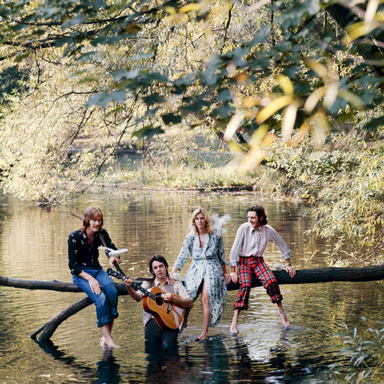 Vier mensen zitten op een boomstam in het water. Eén speelt gitaar.