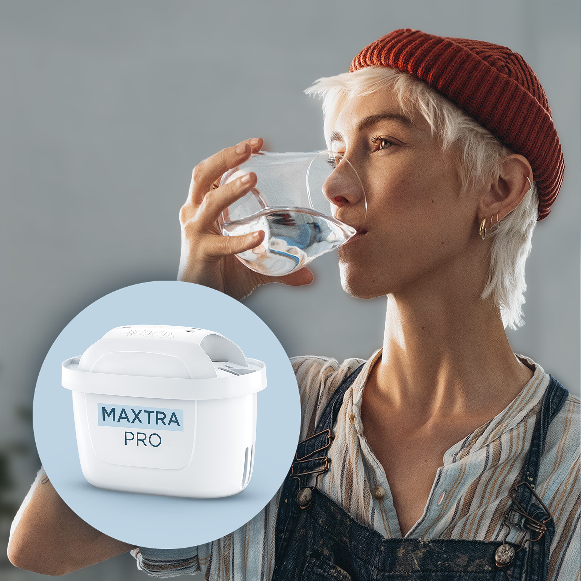 Une femme aux cheveux courts et blancs boit un verre d'eau. Un filtre à eau à côté.