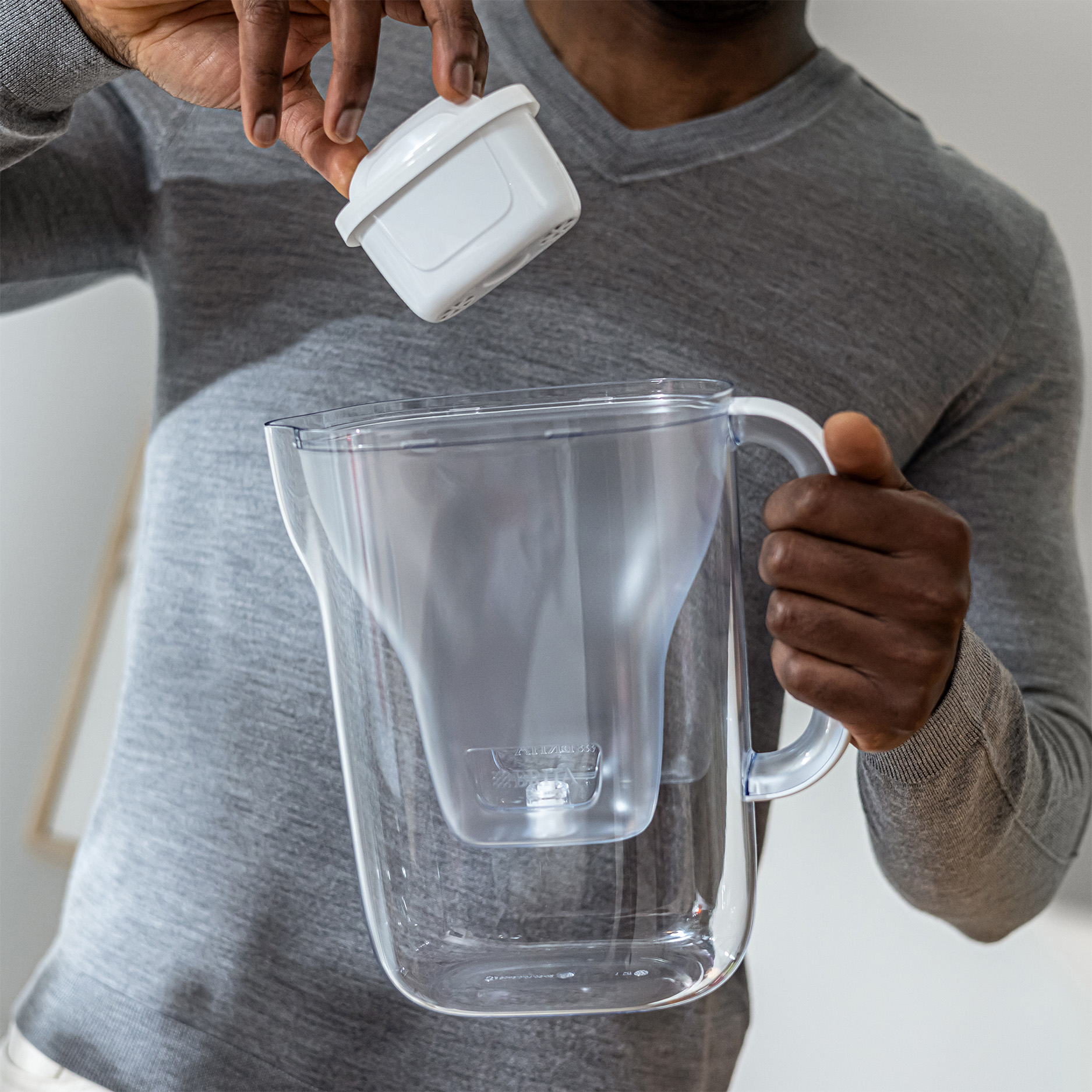 Un uomo inserisce un filtro per l'acqua bianco in una caraffa trasparente.