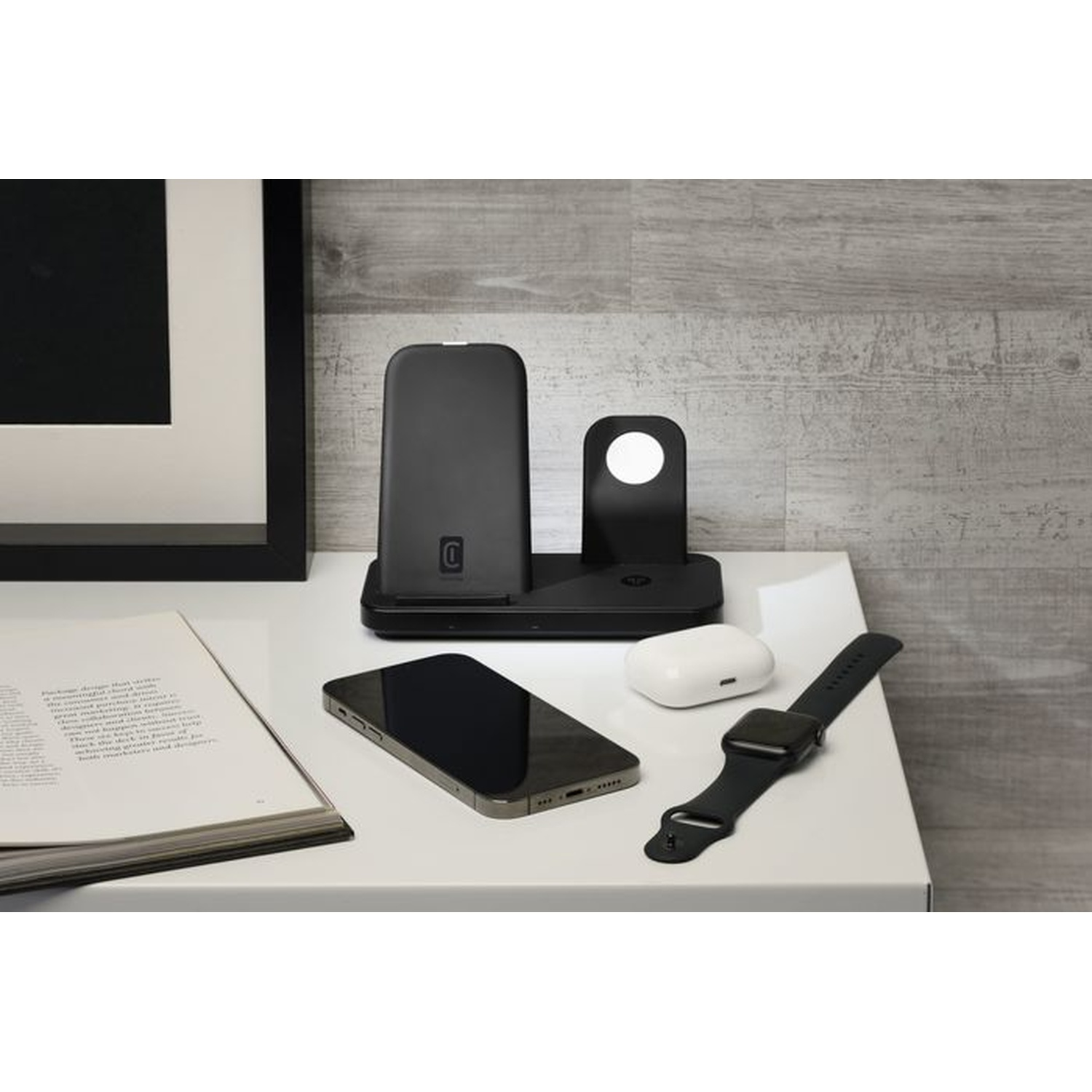 Un caricabatterie nero per più dispositivi con telefono, orologio e auricolari su un tavolo.