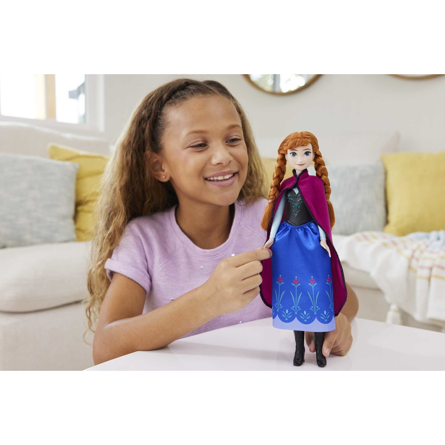 Una bambina sorridente tiene una bambola vestita come Anna di Frozen, con capelli rossi intrecciati.