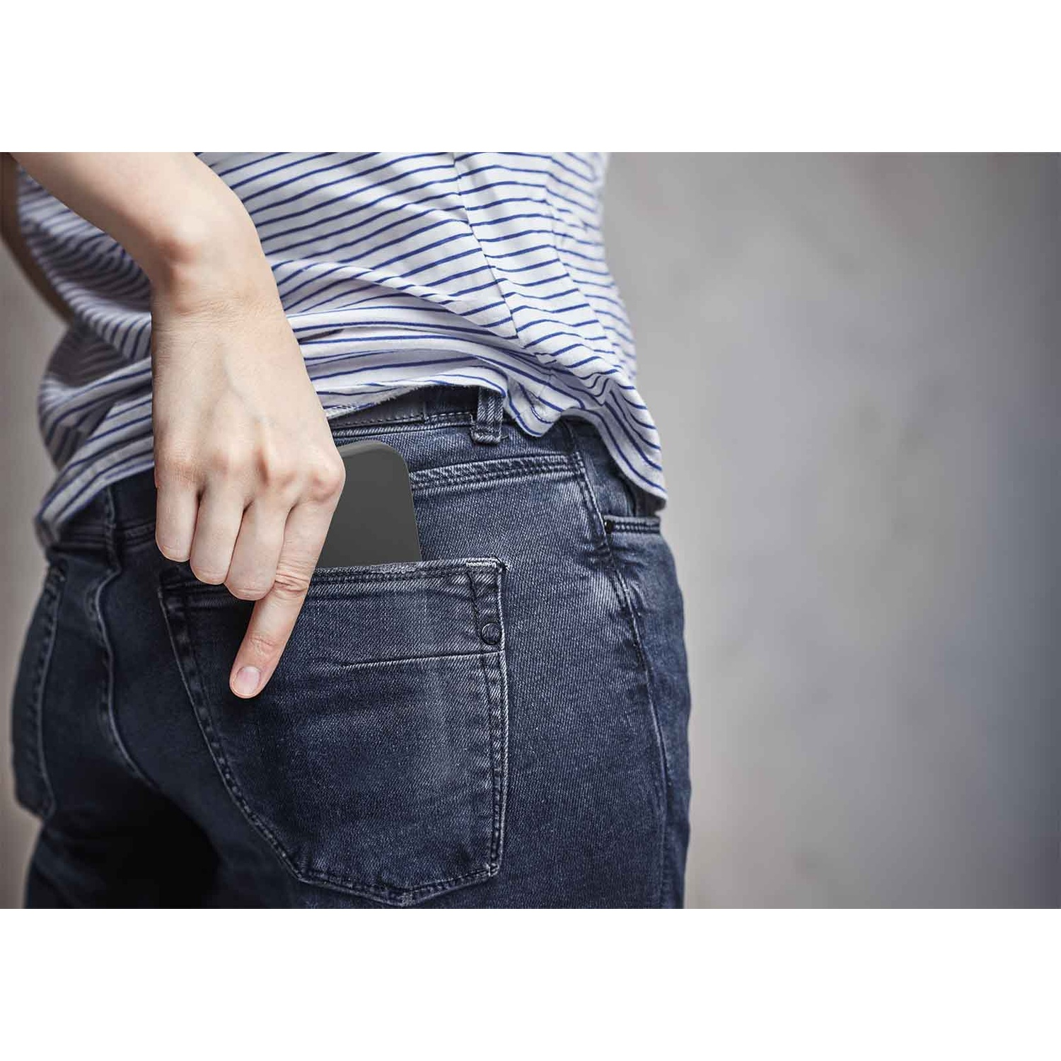 Una mano inserisce un telefono nero nella tasca posteriore di un jeans blu.