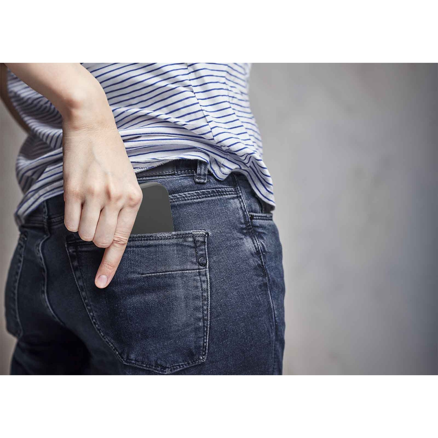 Una persona sta mettendo uno smartphone nero nella tasca posteriore dei jeans.