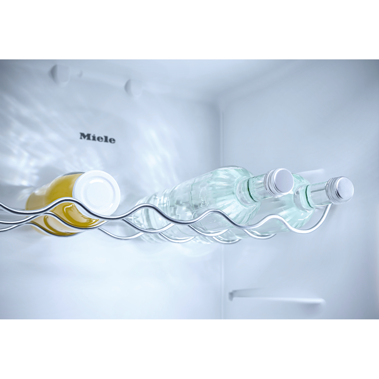 A Miele refrigerator holding two glass bottles of water and one bottle of juice.