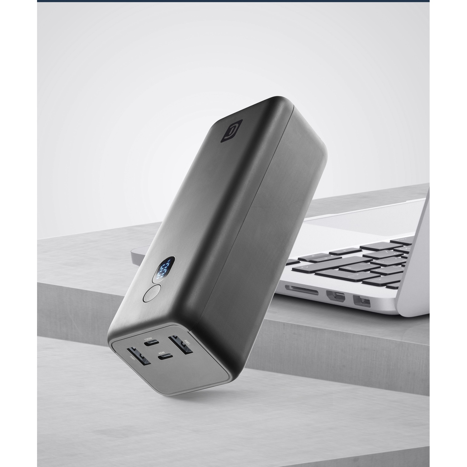 Un caricabatterie power bank nero con porte USB e un laptop accanto.